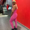 Side profile of fuchsia pink high-waisted leggings and strappy topstanding infront of Virgin Active gym wall