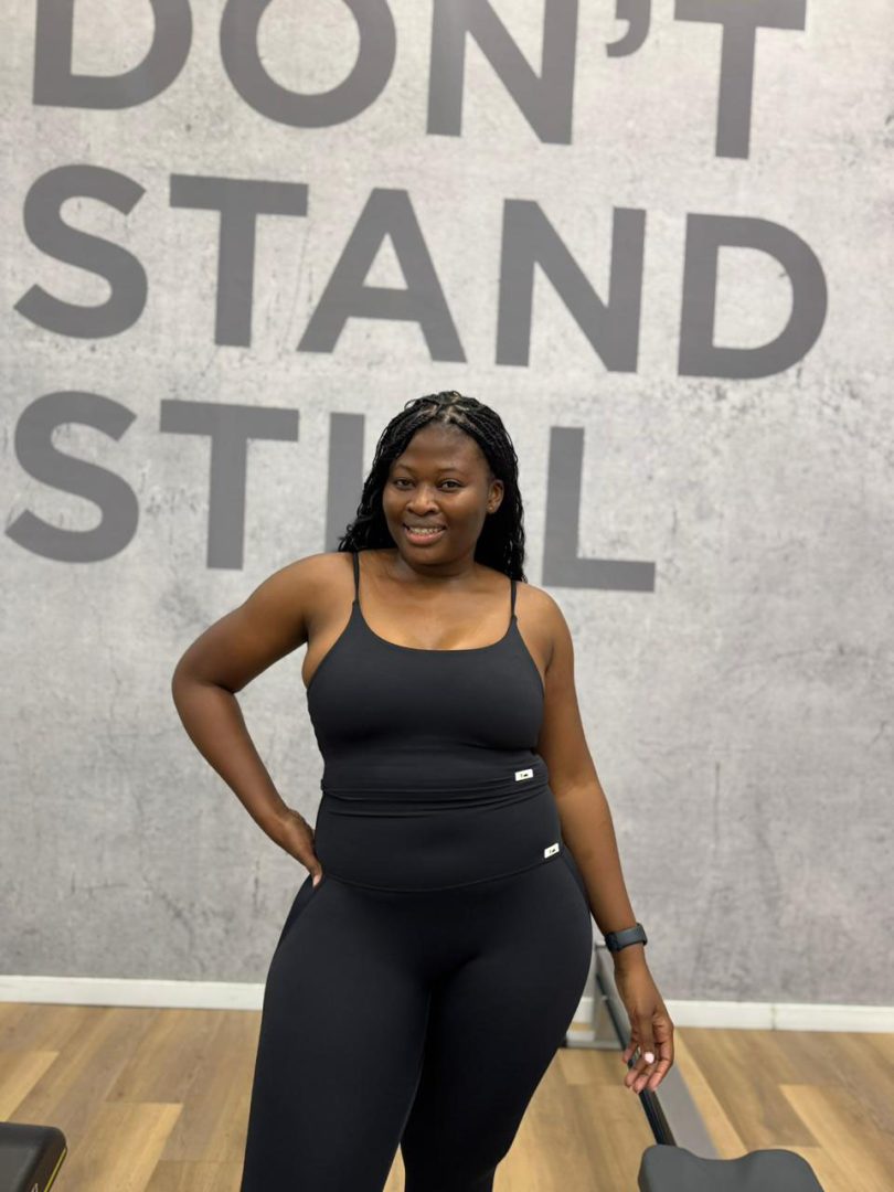 Front view of black Sculpt Mint strappy gym set on a curvy silhouette. Standing in front of a wall written Stand Still