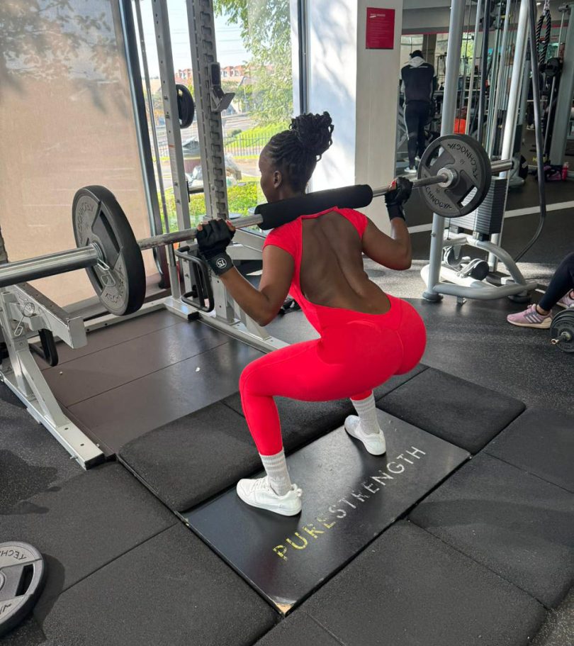Rear view of a woman performing a barbell squat in the red Allure open-back jumpsuit, demonstrating its squat-proof durability.