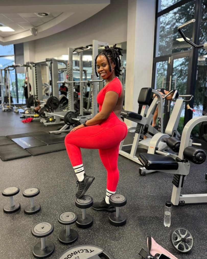 Full-body shot of a woman in the red Allure backless jumpsuit standing in a gym, emphasizing the body-hugging fit.