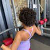 Back view of woman wearing lavender open back athleisure bodysuit using gym machine South Africa