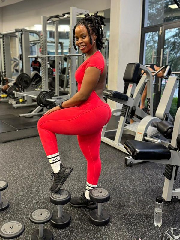 Full-body shot of a woman in the red Allure backless jumpsuit standing in a gym, emphasizing the body-hugging fit.